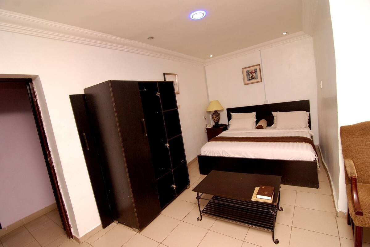 Una habitación de hotel con cama, armario, mesita de noche con lámpara y una silla.