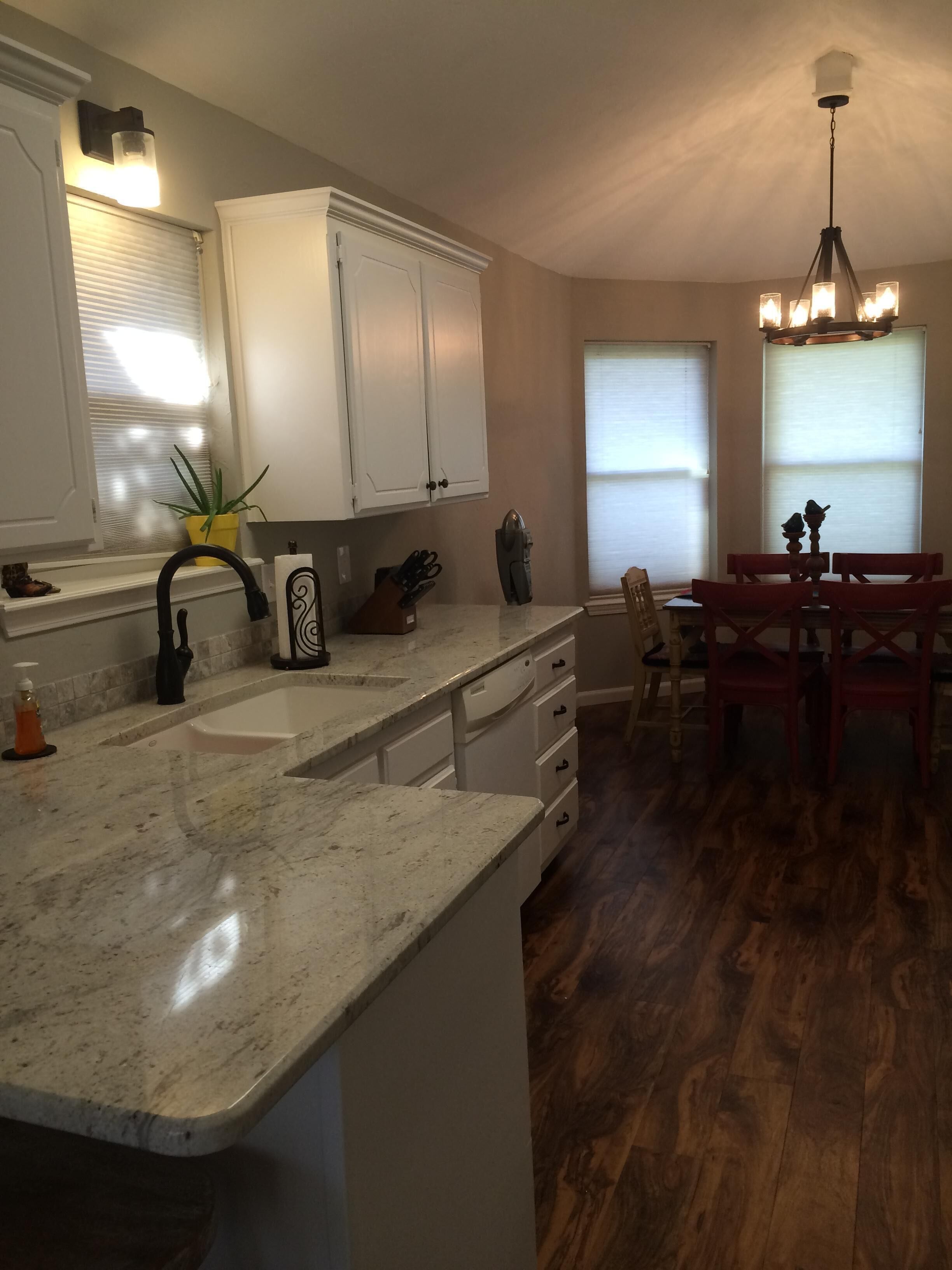 A kitchen with white cabinets, a marble countertop, a sink, and a dining area with a wooden table and chairs.