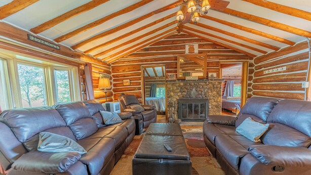 A log cabin interior with two leather sofas, a stone fireplace, and a chandelier. - Republic Island -Summer Paradise – Your Private Island Awaits! (Republic)