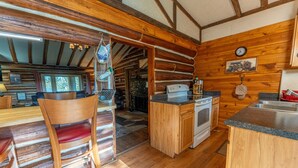 A rustic cabin interior with a wooden dining area, a kitchen with a stove and sink, and a wooden ceiling with exposed beams. - Republic Island -Summer Paradise – Your Private Island Awaits! (Republic)