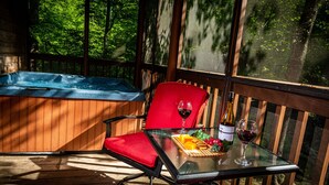 Terraza de madera con mesa de vidrio, una silla roja y un jacuzzi.