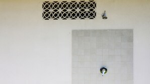Pareti doccia in piastrelle con soffione e griglia di ventilazione.