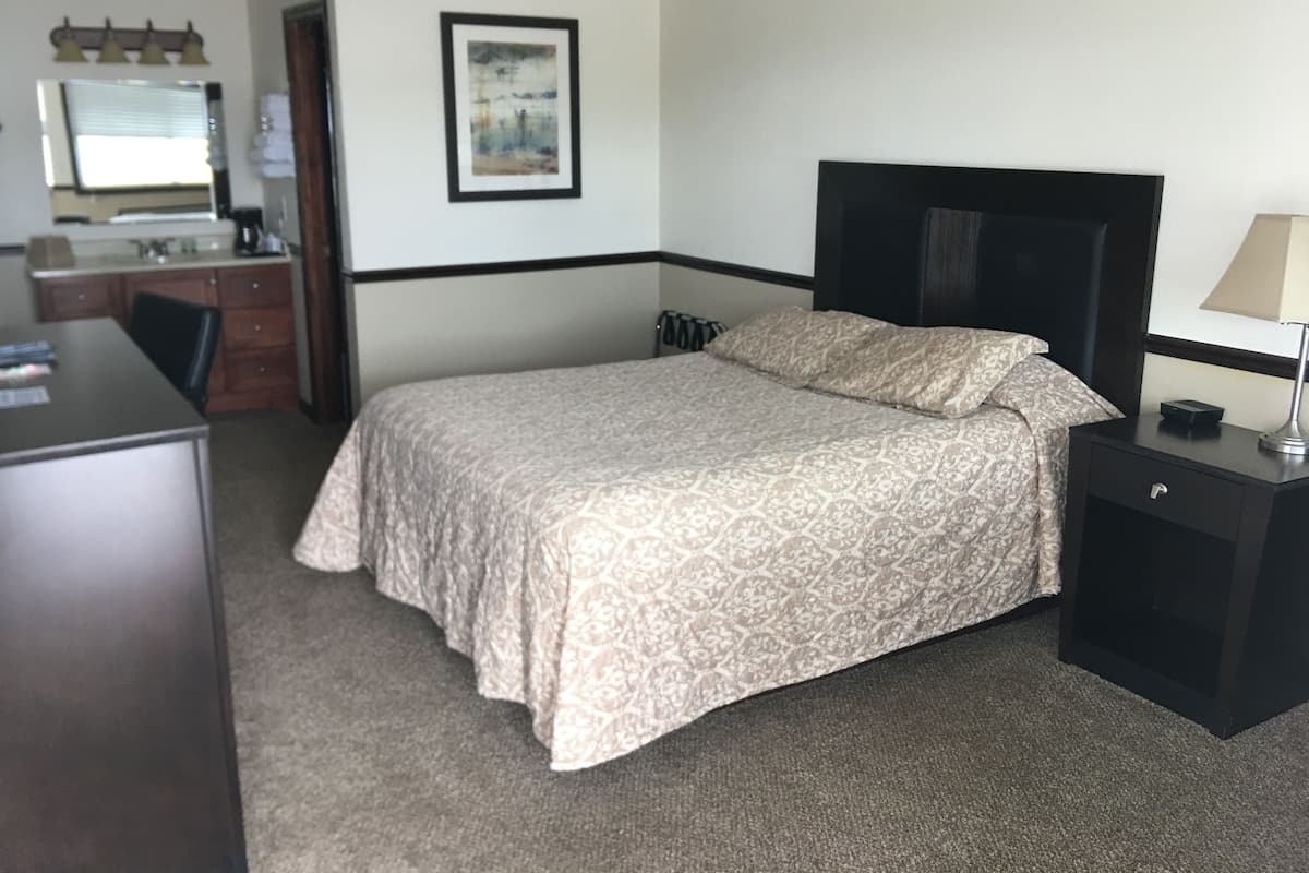 Una habitación de hotel con cama, escritorio, silla, lámpara y un cuadro en la pared.