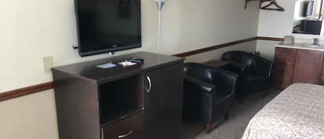 Une chambre d’hôtel comprenant un lit, un bureau avec une télévision, une lampe et deux chaises.