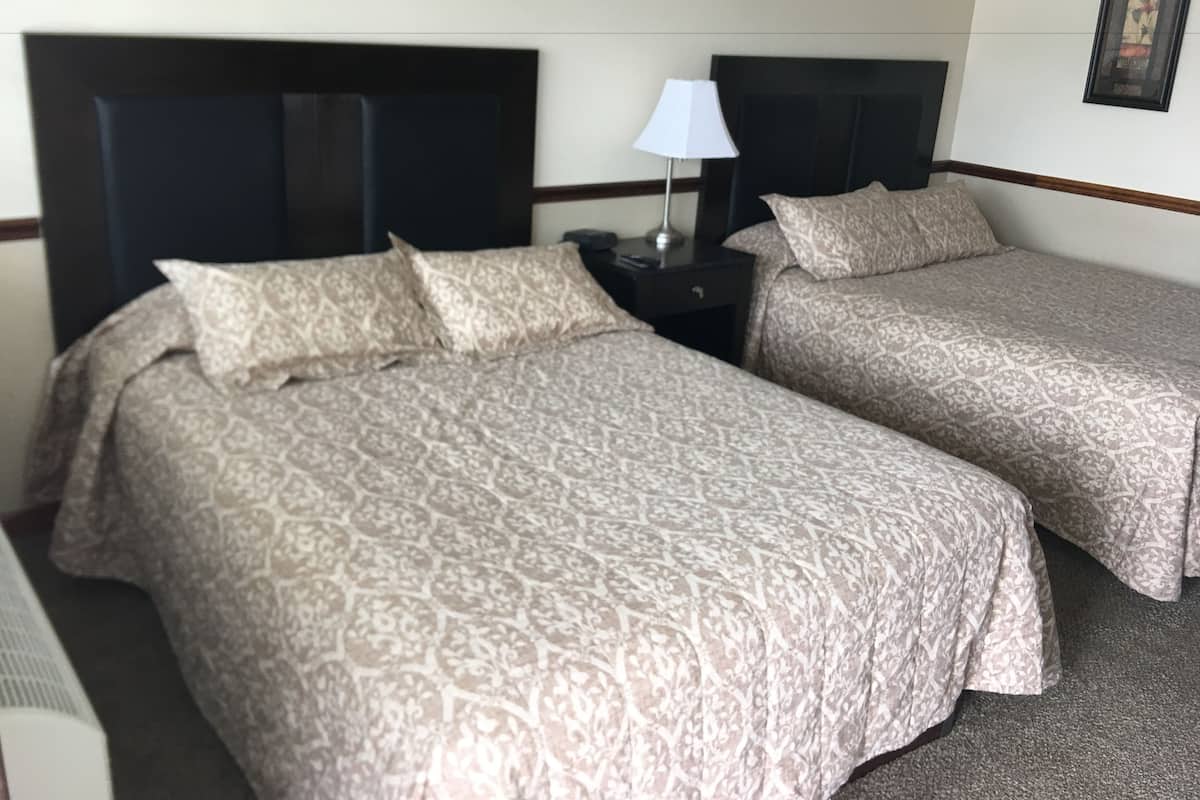 Una habitación de hotel con dos camas, una mesita de noche con lámpara y un cuadro enmarcado en la pared.