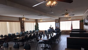A large dining area with multiple tables and chairs, ceiling fans, and a brick wall. - Flag's West Motel (Downey)