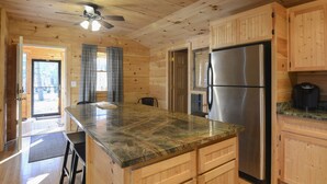 A wooden cabin interior with a kitchen featuring a granite countertop, stainless steel refrigerator, and wooden cabinets. - Newly Renovated Rustic Cabin   (Tamworth)
