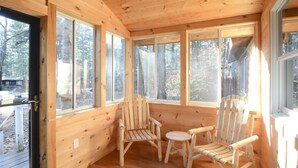A wooden cabin interior with large windows, two wooden chairs, and a small table. - Newly Renovated Rustic Cabin   (Tamworth)
