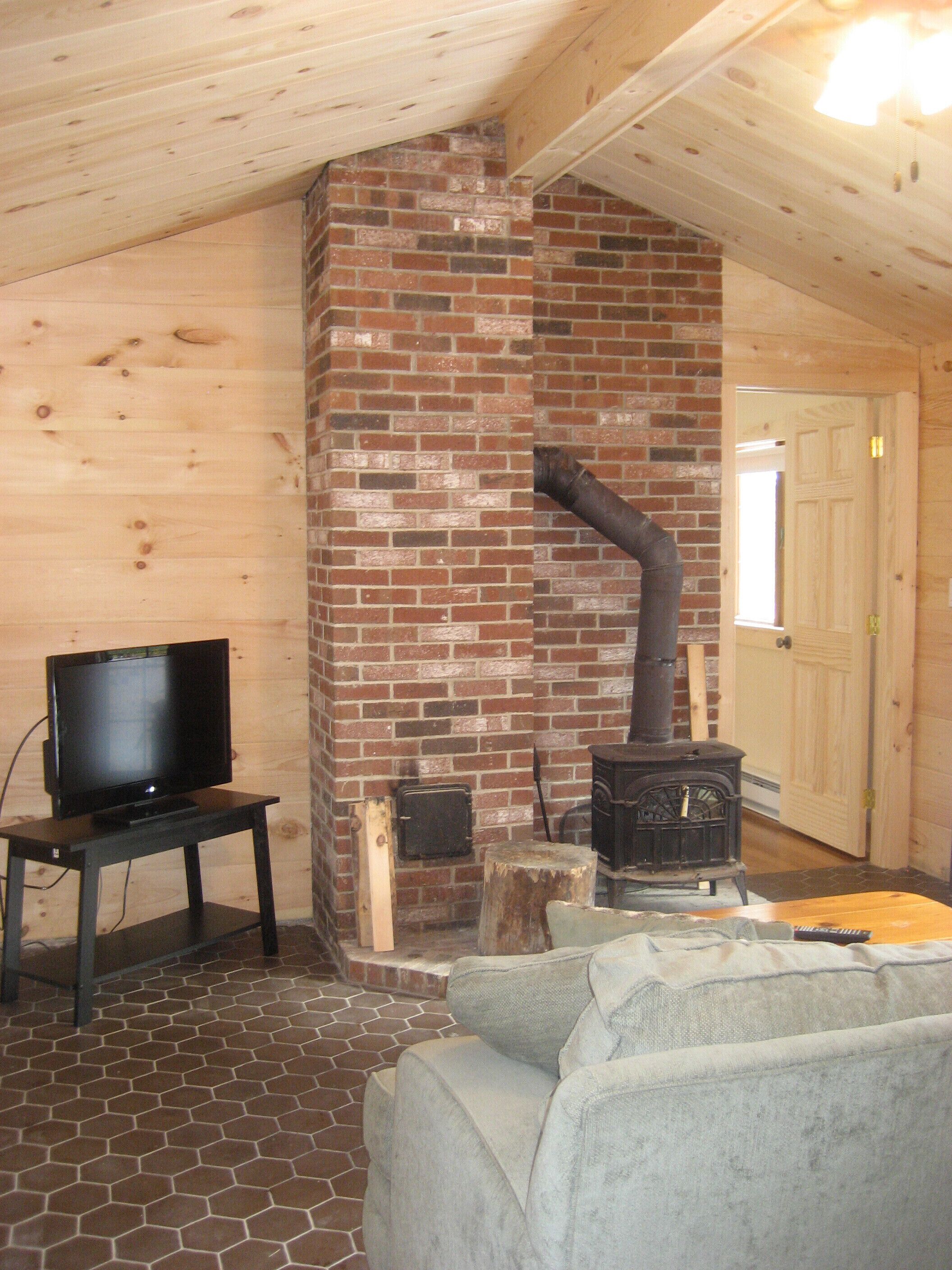 A cozy room with a brick fireplace, a television on a stand, and a couch.