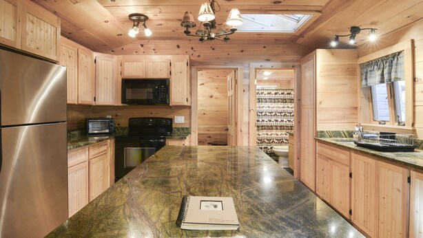 A kitchen with wooden cabinets, a stainless steel refrigerator, a microwave, and a large island with a notebook and keys. - Newly Renovated Rustic Cabin   (Tamworth)