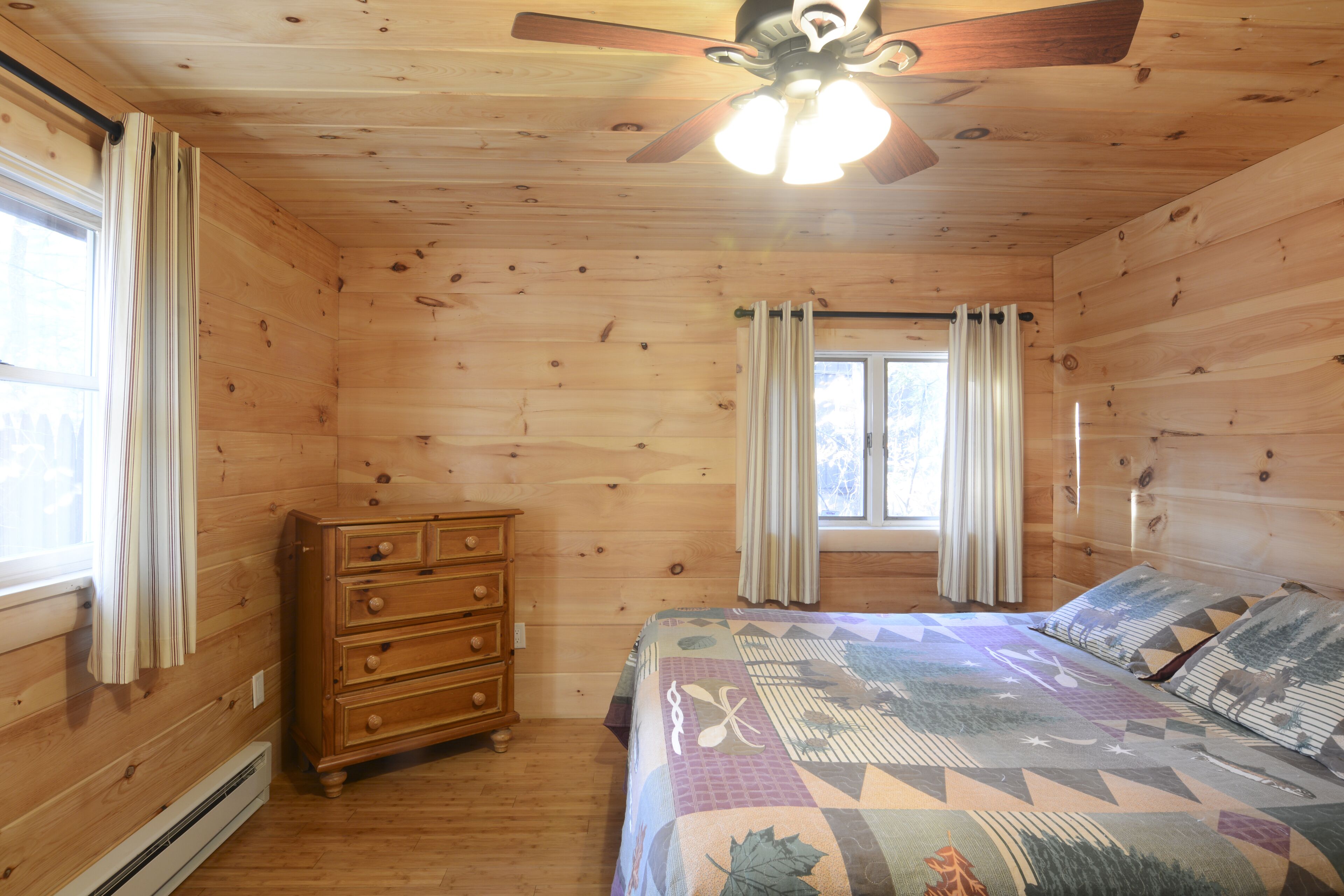 Dormitorio de cabaña de madera con cama, cómoda y ventilador de techo.