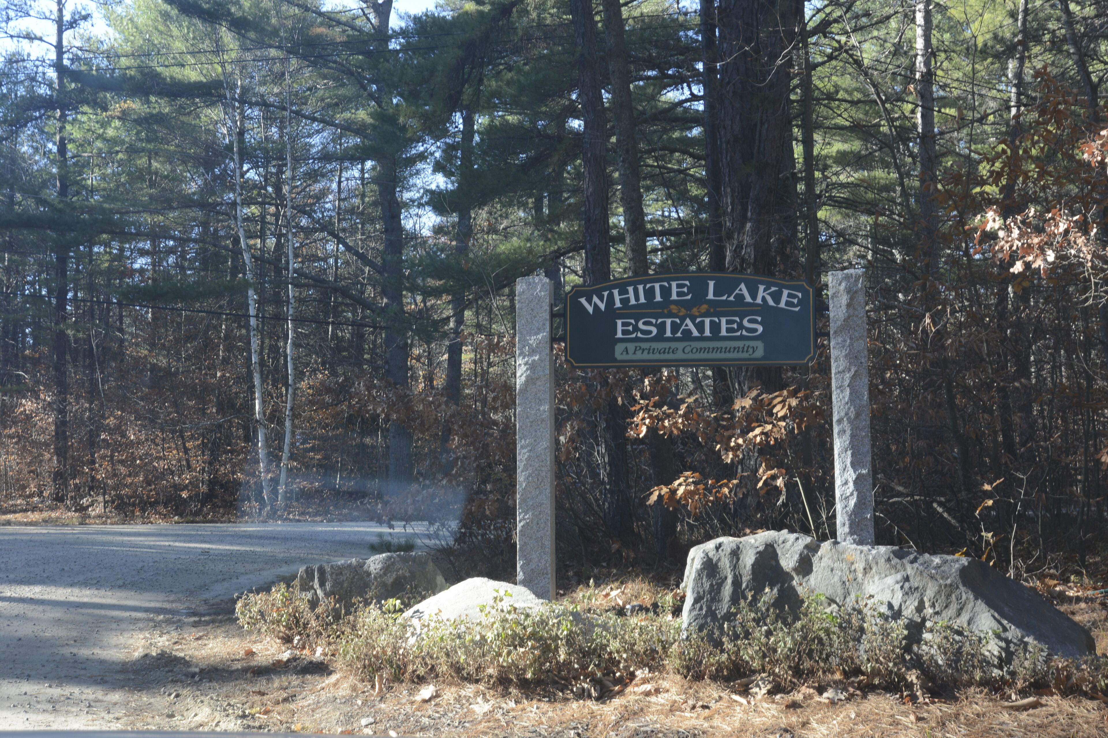 A sign for White Lake Estates, a private community, surrounded by trees and a dirt road.