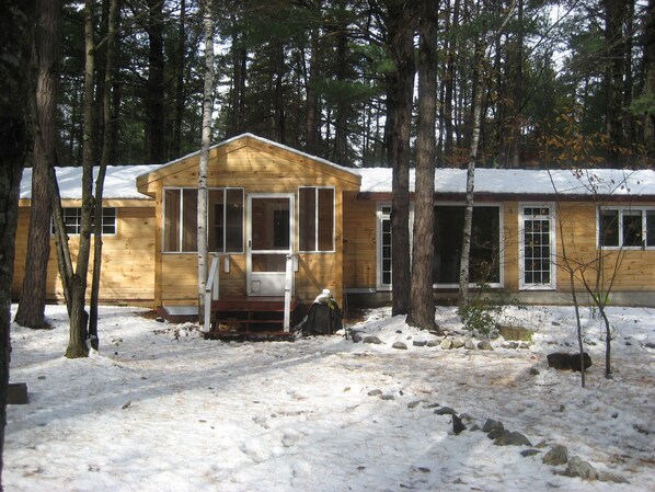 A wooden cabin with a porch, surrounded by trees and covered in snow.