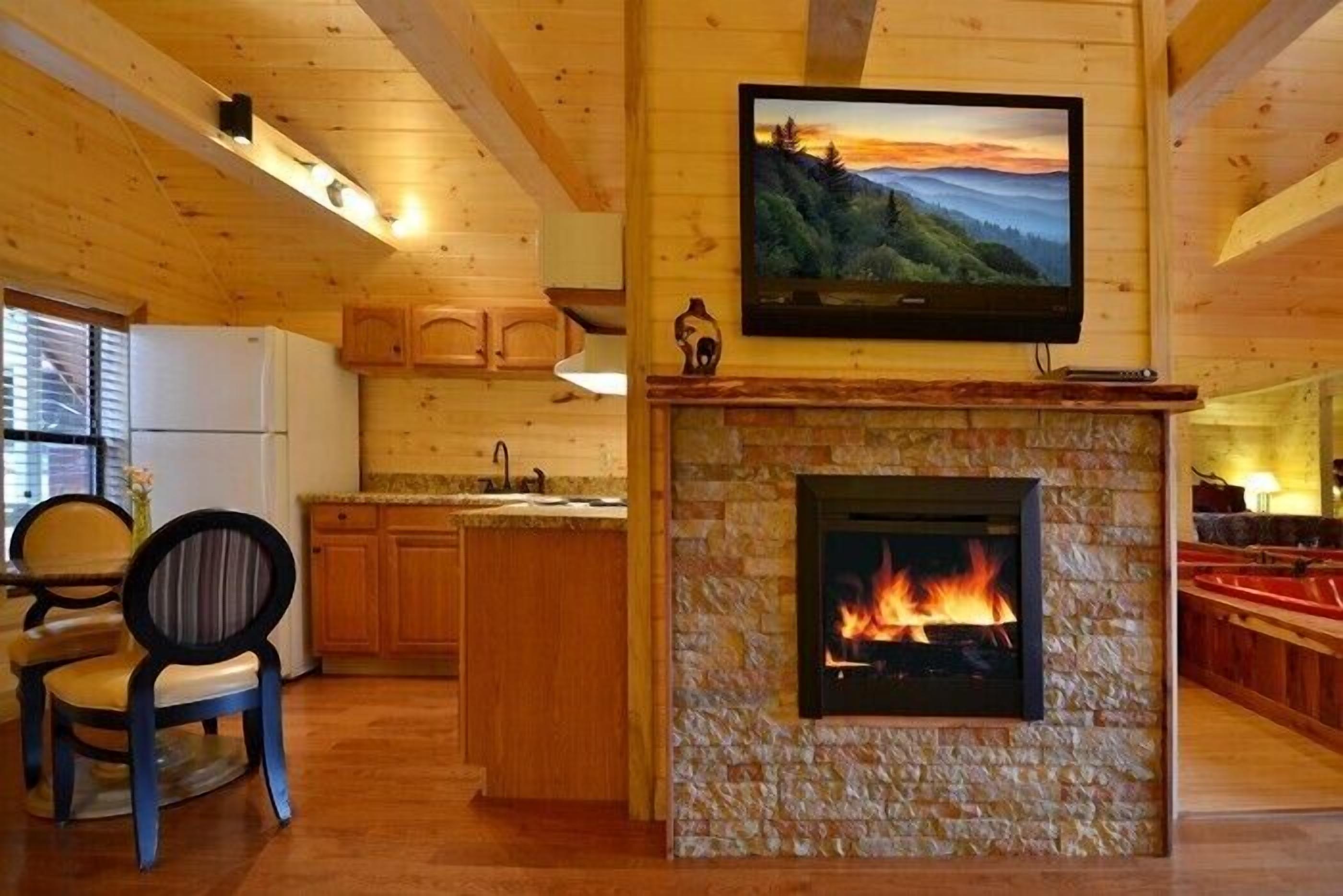 Un intérieur de chalet chaleureux avec une cheminée en pierre, des poutres en bois au plafond, un coin cuisine et un espace repas.