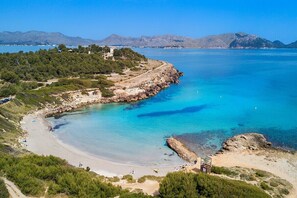 A coastal landscape with a beach, clear blue waters, and a mountainous backdrop.