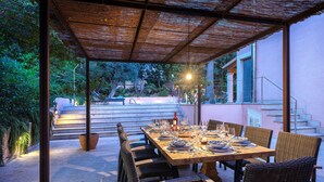 An outdoor dining area with a wooden table set for six, surrounded by wicker chairs, under a thatched roof. - Villa Elvissa by Balearic Villas (Alcúdia)