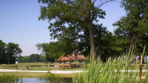 A tranquil outdoor setting with a pond, purple flowers, and a gazebo. - Pleasant Grove Inn (Linton)
