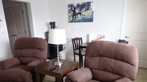 A living room with two brown armchairs, a small table, a lamp, and a painting on the wall. - Pleasant Grove Inn (Linton)