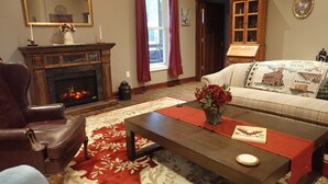 A living room with a fireplace, a sofa, a coffee table, and a red rug. - Pleasant Grove Inn (Linton)