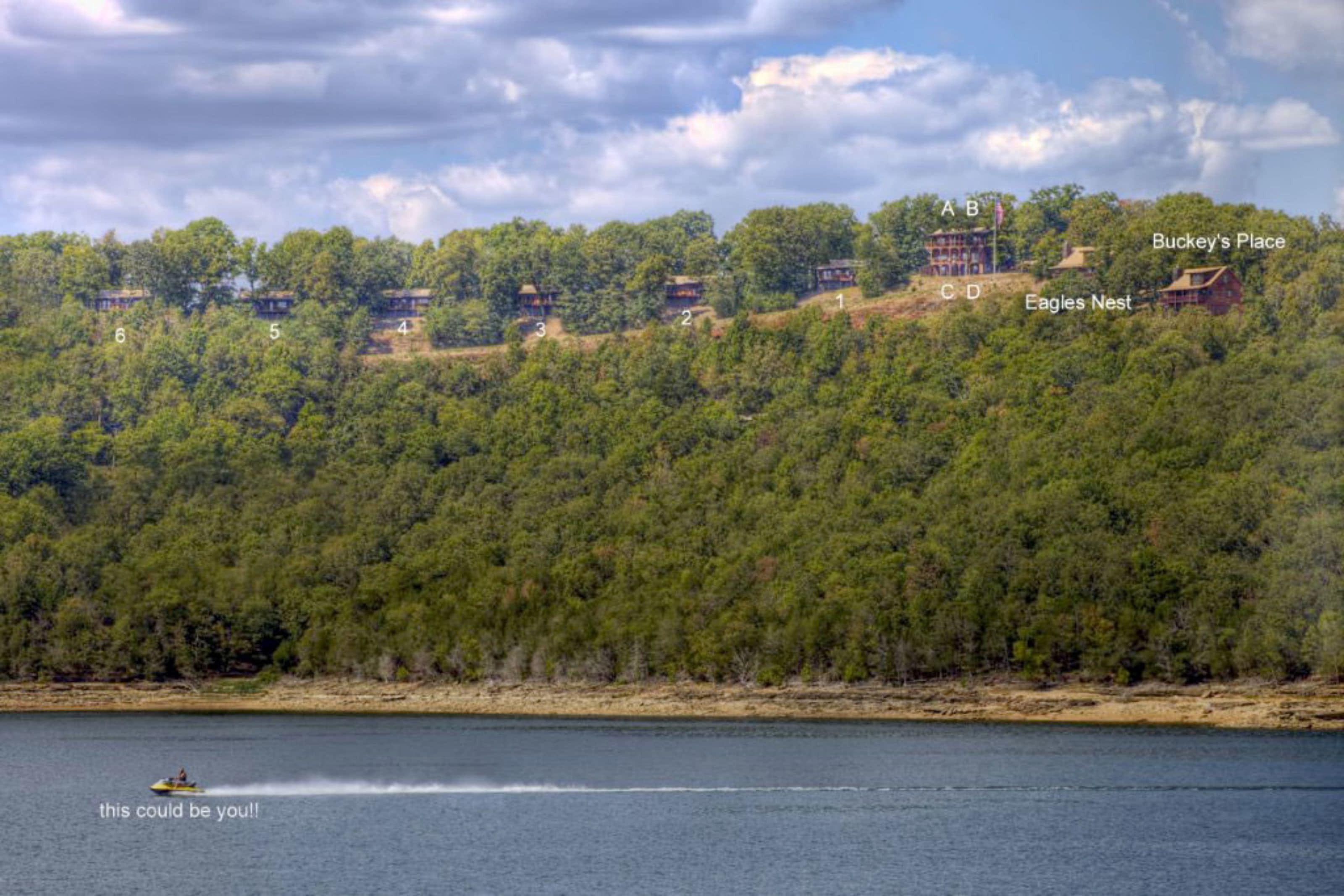 A lakeside property with numbered cabins, a boat on the water, and a view of the surrounding forest.