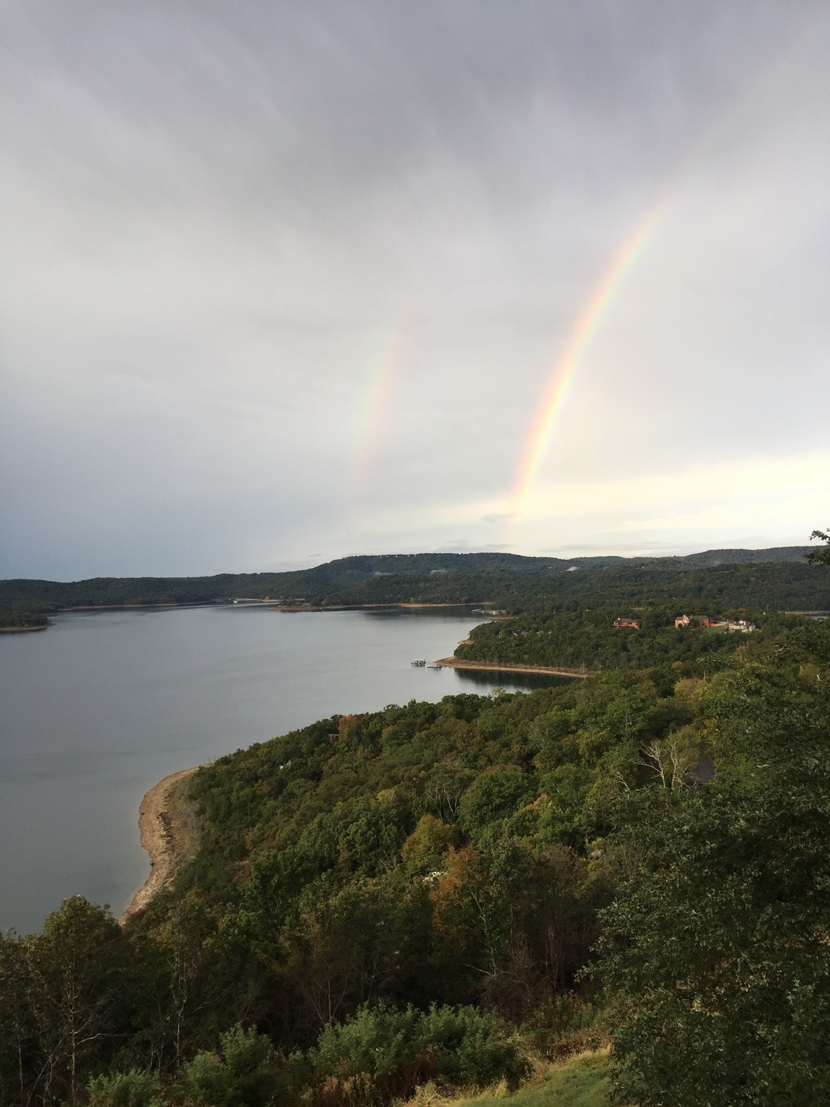A landscape with a lake, forested hills, and a rainbow.