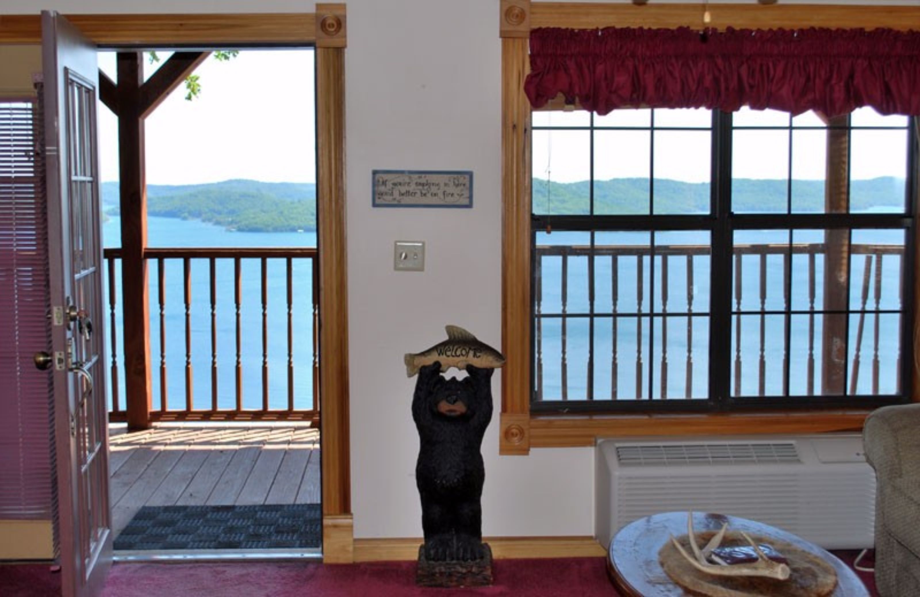 A room with a wooden deck, a view of a lake, a bear statue, and a sign on the wall.
