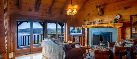 A spacious living room with a fireplace, wooden floors, and a large window overlooking a scenic view.