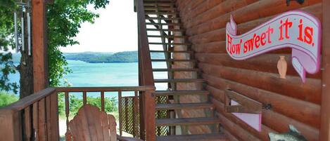 A wooden staircase leading to a deck with a view of a lake, a wooden chair, and a sign that says "How sweet it is."