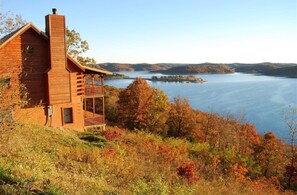 A rustic cabin with a balcony overlooking a lake, surrounded by autumn foliage.