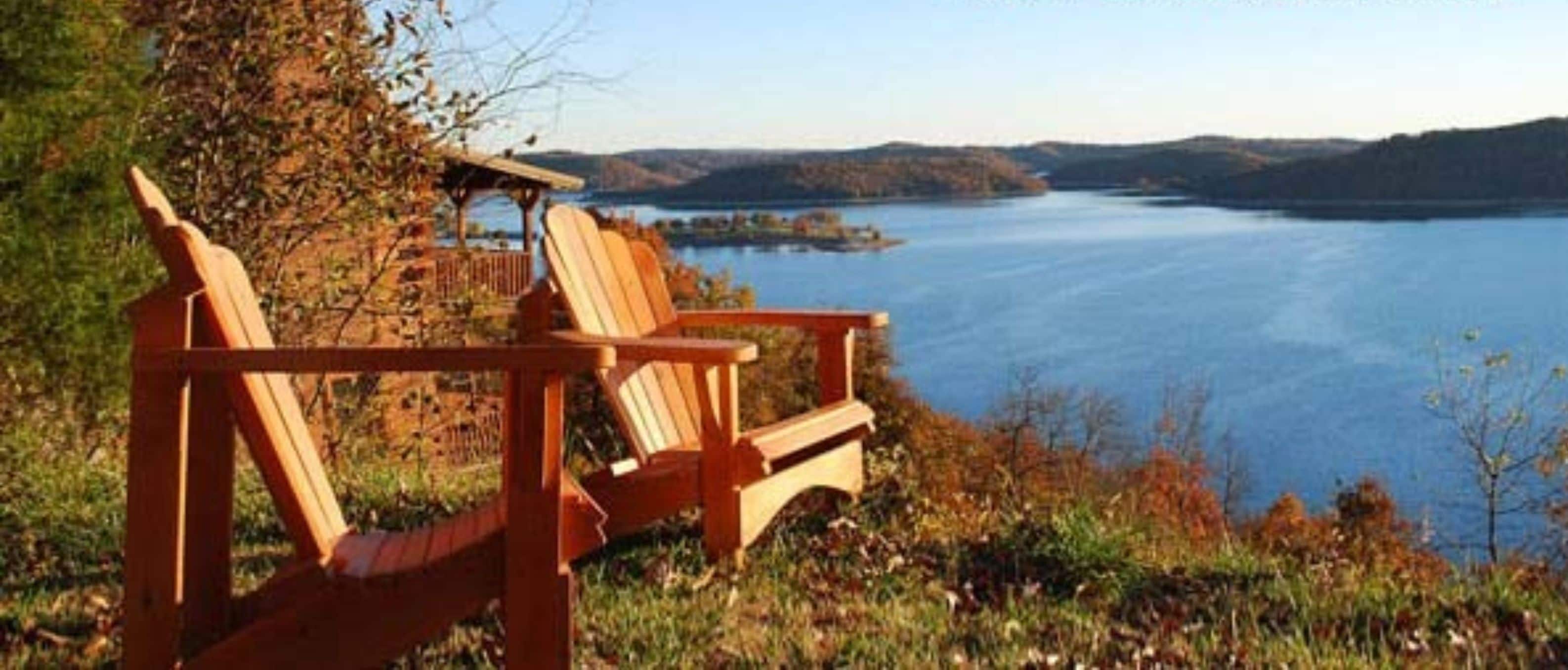Zwei Holz-Adirondack-Stühle, die auf einen See mit einer entfernten Uferlinie zeigen.