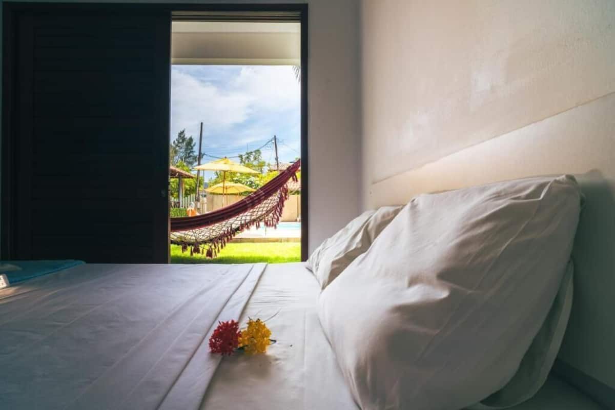 Une chambre d’hôtel avec un lit, une vue sur un hamac à l’extérieur et une fenêtre.