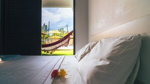 Ett hotellrum med en säng, utsikt över en hängmatta utanför och ett fönster.