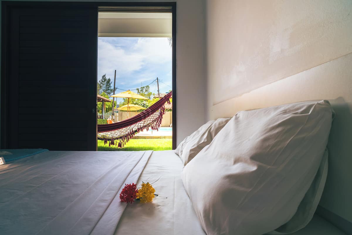 Une chambre d’hôtel avec un lit, une vue sur un hamac à l’extérieur et une fenêtre.