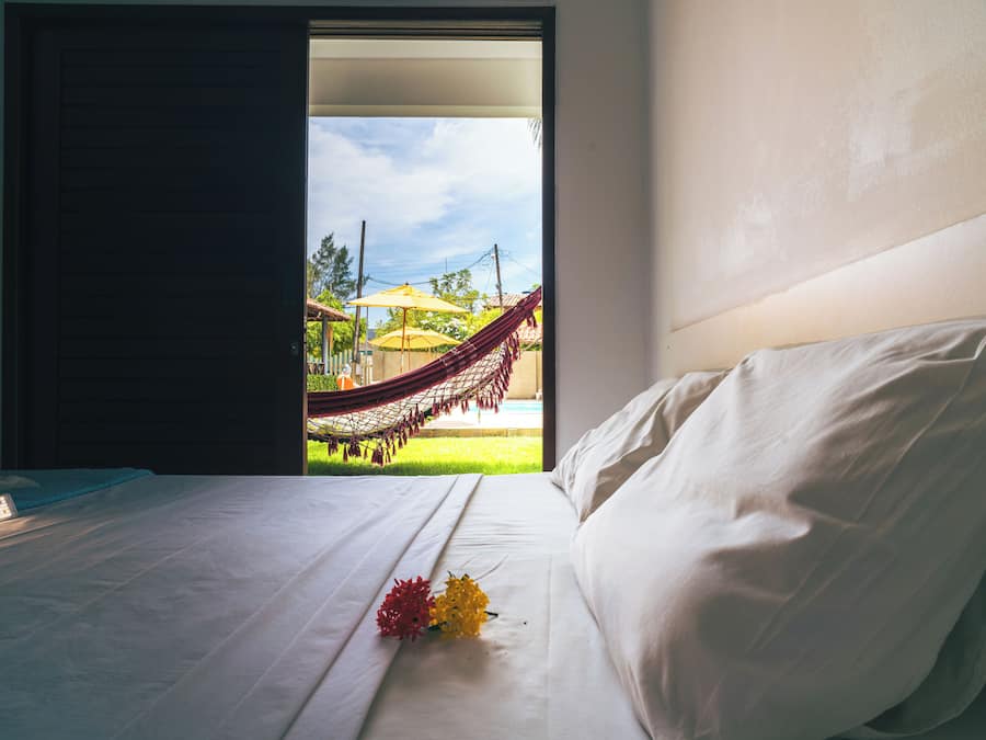 Una habitación de hotel con una cama y vista a una hamaca en el exterior, además de una ventana.
