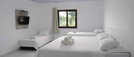 A hotel room with two beds, a flat-screen TV mounted on the wall, and a window with a view of greenery.