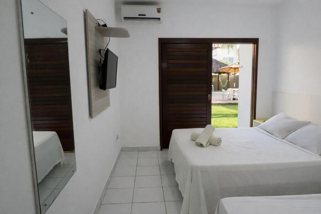 A hotel room with two beds, a TV, and a door leading to an outdoor area with a pool and umbrellas.
