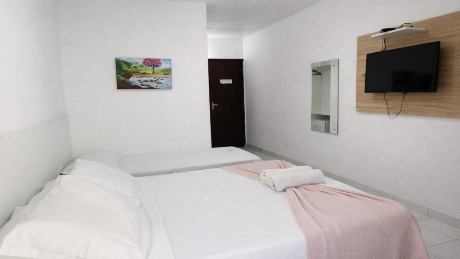 A hotel room with two beds, a painting, a television, and a door.