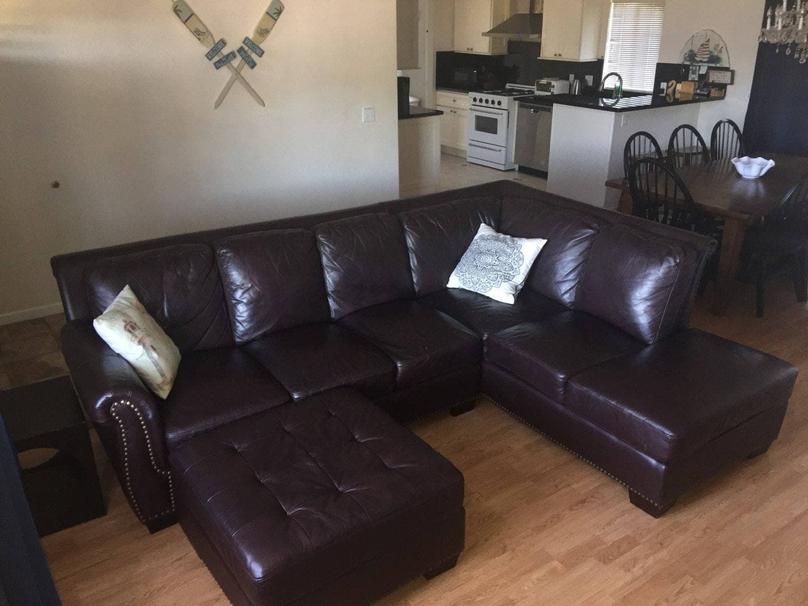 A dark brown leather sectional sofa with a matching ottoman, a dining table with chairs, and a kitchen area with appliances.