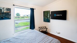 A hotel room with a bed, a window with curtains, a chair, a wall-mounted TV, and a framed picture.