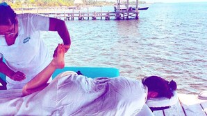 A massage therapy session on a wooden deck by the water, with a thatched-roof structure in the background. - An unBELIZEable home...Barefoot beachfront luxury! (San Pedro)