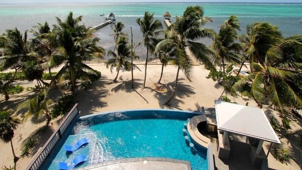 A pool area with a view of the ocean, surrounded by palm trees and a sandy beach. - An unBELIZEable home...Barefoot beachfront luxury! (San Pedro)