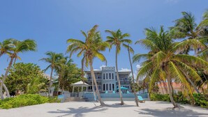 A beachfront property with a two-story building, palm trees, and a clear blue sky. - An unBELIZEable home...Barefoot beachfront luxury! (San Pedro)