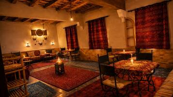 Una habitación acogedora, con luz tenue, vigas de madera, un sofá, una mesa de comedor con sillas y una alfombra estampada.
