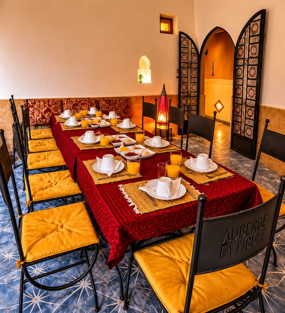 A dining area with a long table set for breakfast, featuring yellow cushioned chairs and red tablecloths.