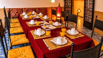 A dining area with a long table set for breakfast, featuring yellow cushioned chairs and red tablecloths.