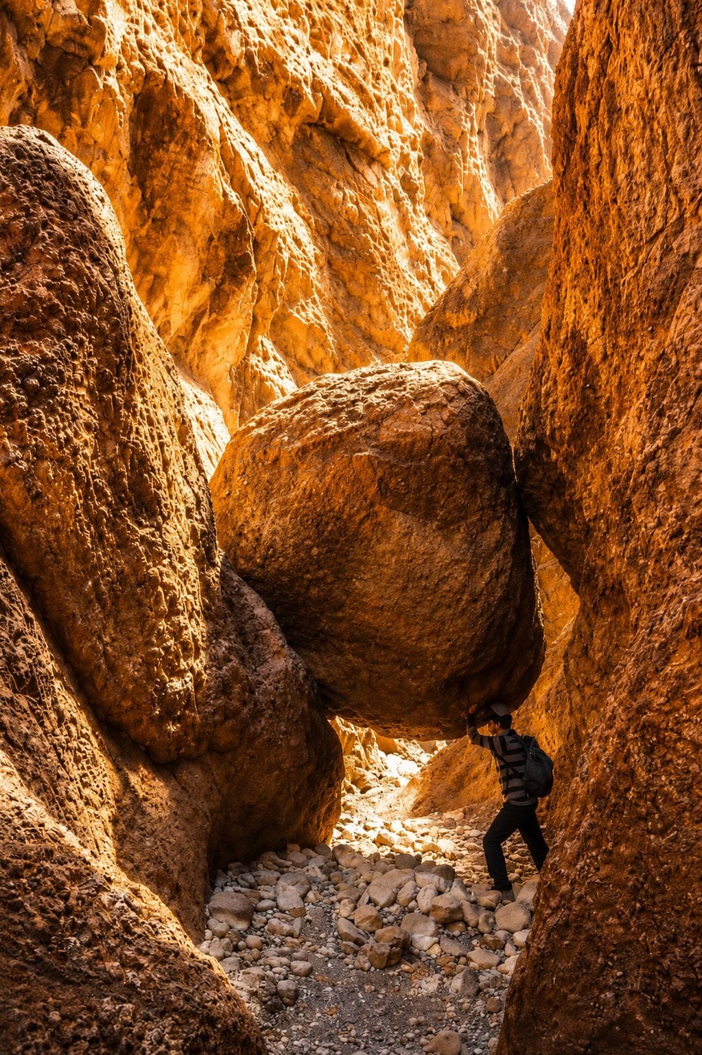 Une personne pousse un énorme rocher dans un étroit canyon, un terrain rocheux parsemé de gros blocs.
