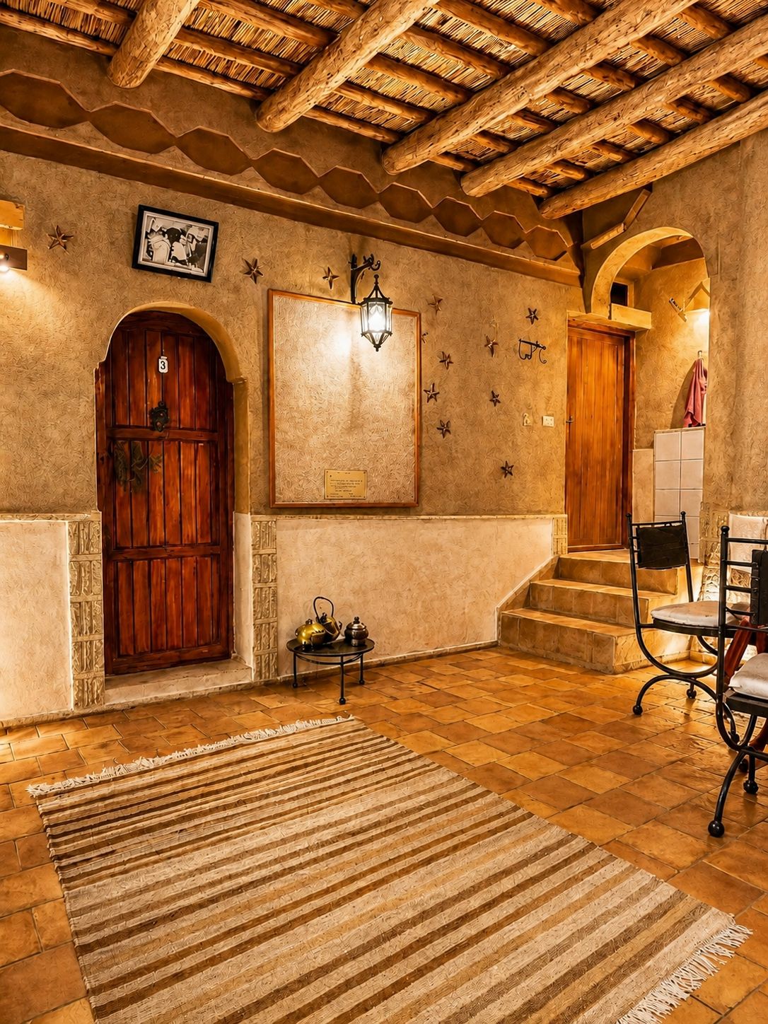 A room with a wooden door, a framed picture, a wall-mounted light fixture, and a staircase leading to another area.