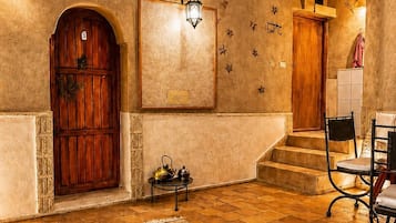 A room with a wooden door, a framed picture, a wall-mounted light fixture, and a staircase leading to another area.