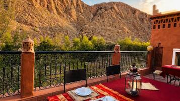 An outdoor dining area with a table set for two, overlooking a mountainous landscape.