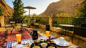 Un espace de restauration en plein air avec une table dressée pour le petit-déjeuner, entouré d’un paysage montagneux pittoresque.